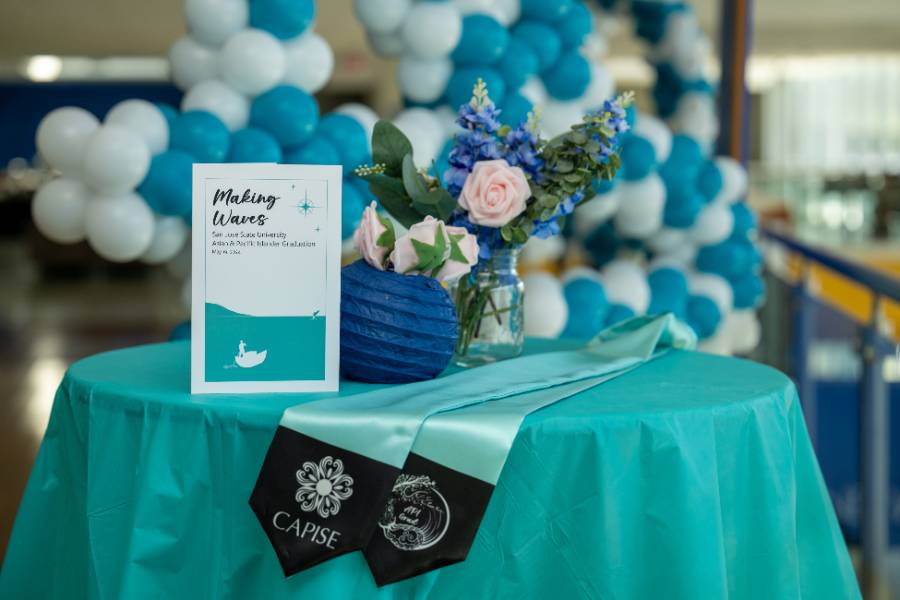 Round table with blue tablecloth and flower centerpiece with API Graduation program and API Graduation stole displayed on table.