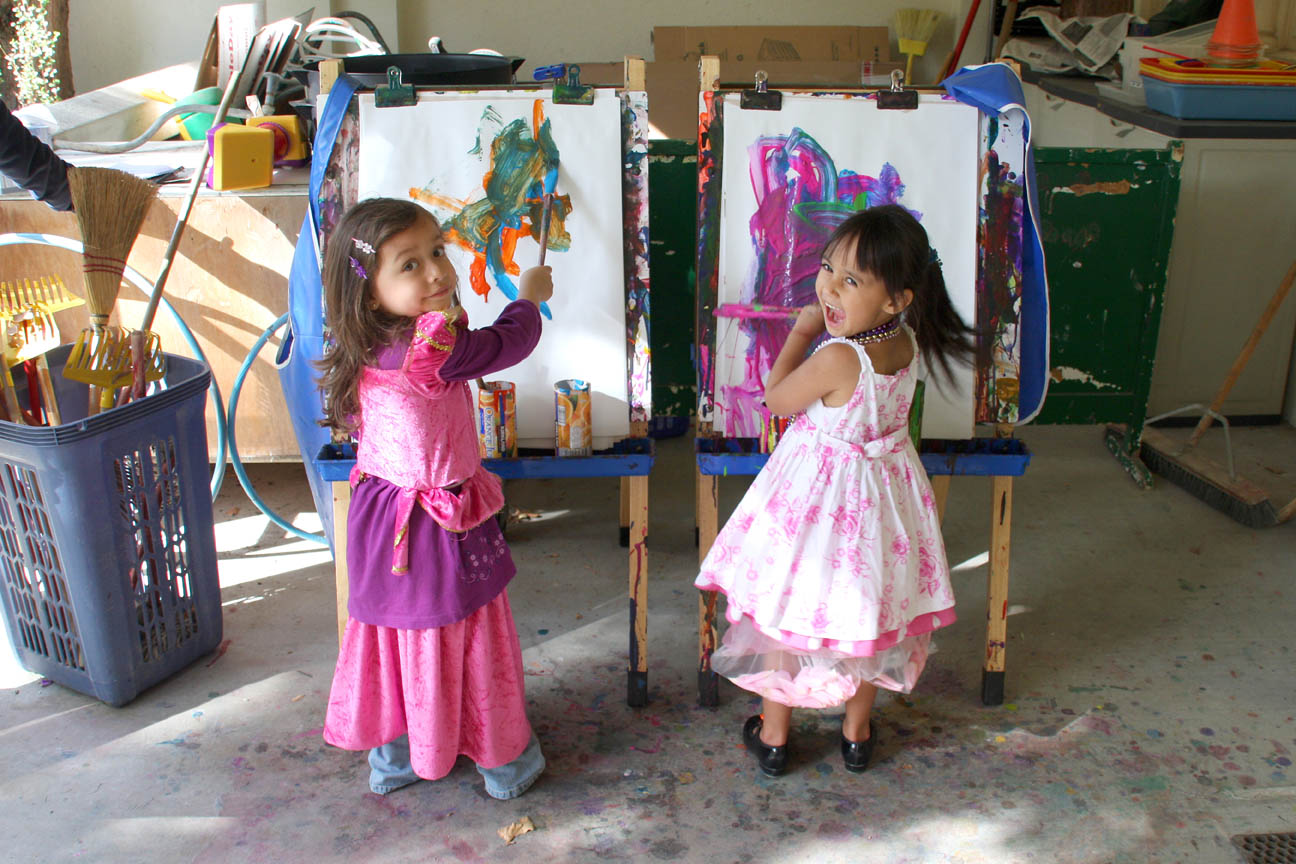Two young girls wearing colorful dresses and painting on easels