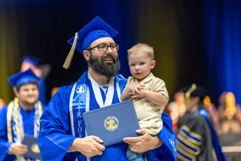 Graduating student holding a child and a diploma
