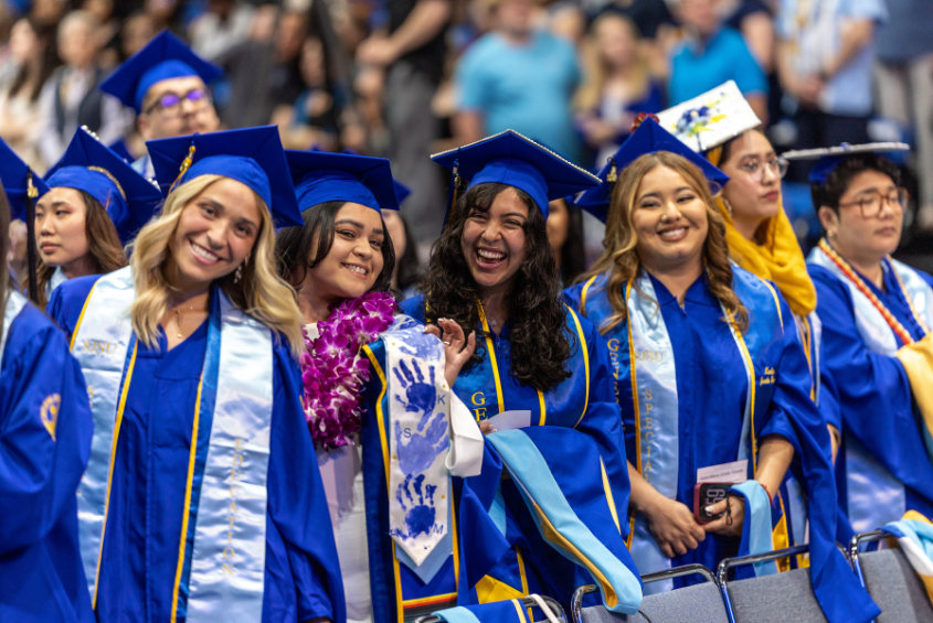 Graduate women smiling for a photograph in the Event Center.