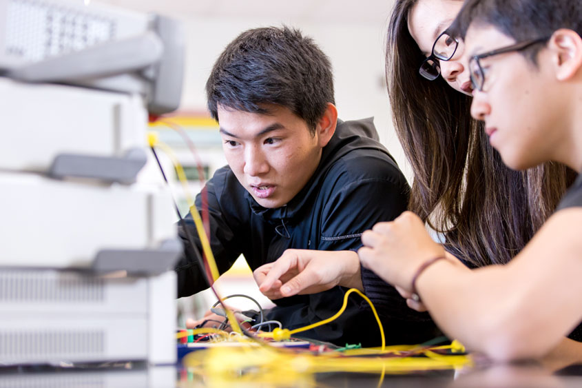 Three engineering students talking and looking at computer equipment boxes.