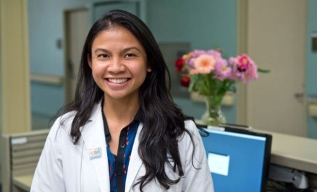 Mae Lavente Dizon, DNP alumni, in a white coat, standing at her place of work.