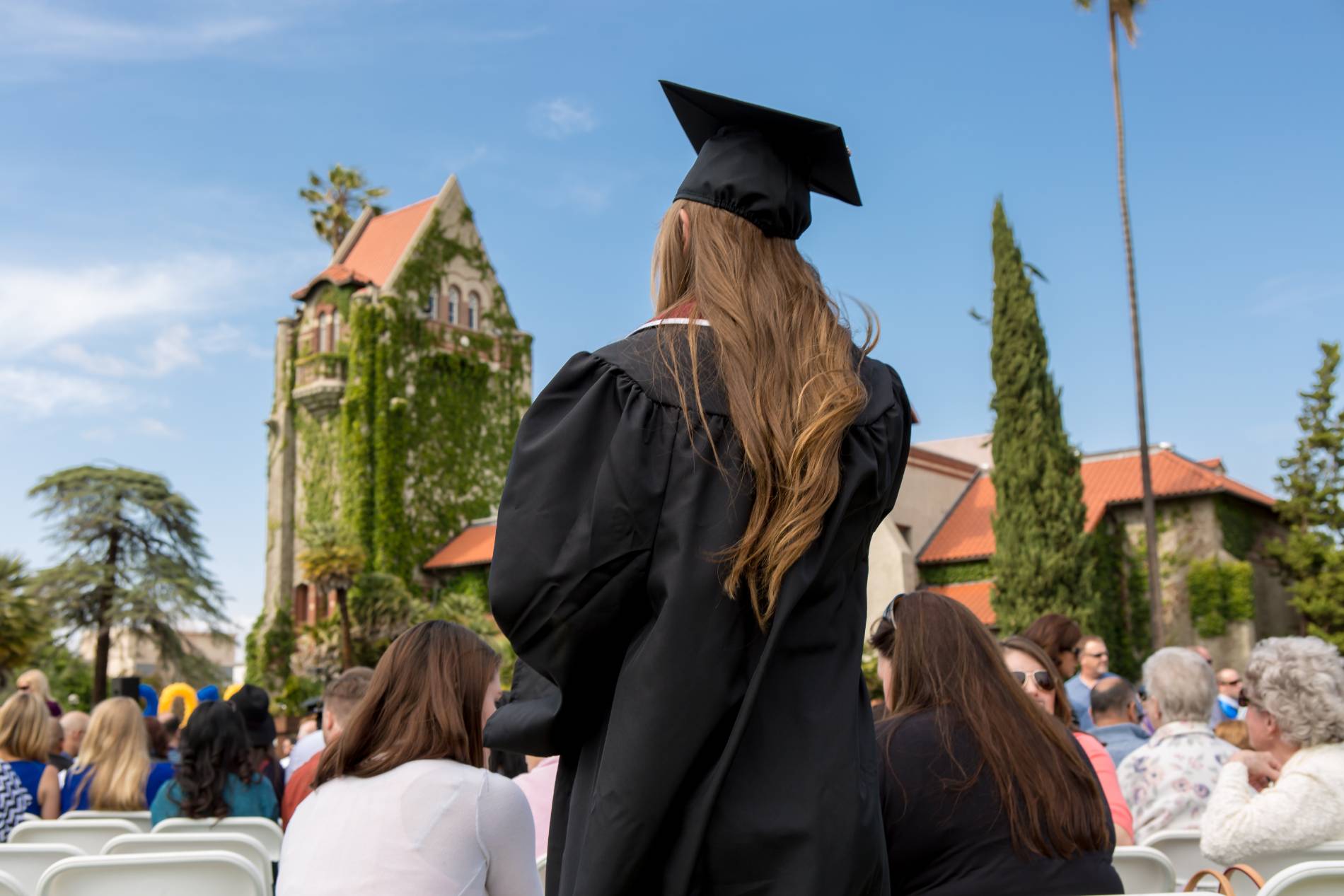 female sjsu graduate stands amongst crowd in front of SJSU's Tower Hall