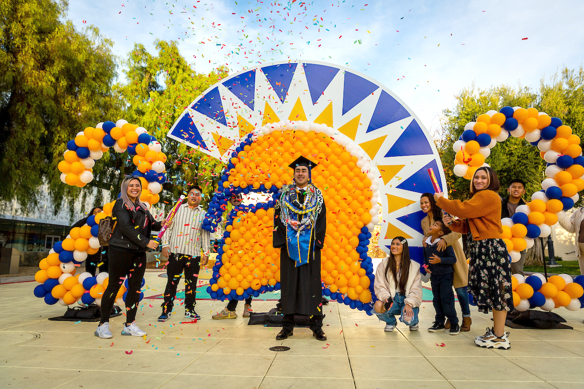 SJSU graduated posing in front of balloon spirit mark with friends shooting confetti in the air 