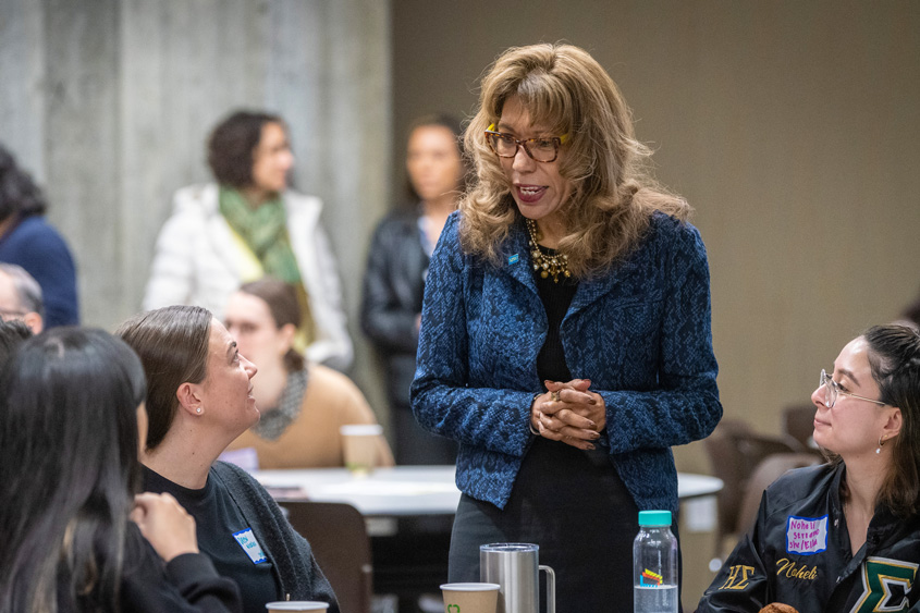 President Teniente-Matson speaking with students at a table.