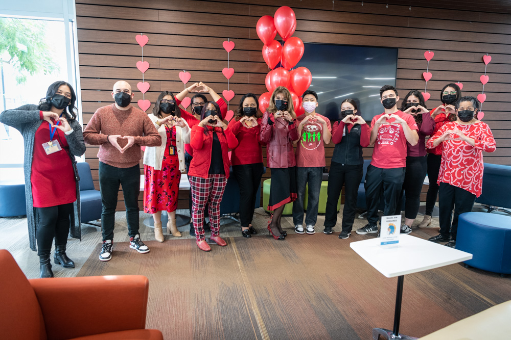 SJSU president with students and staff making a heart sign with their hands.