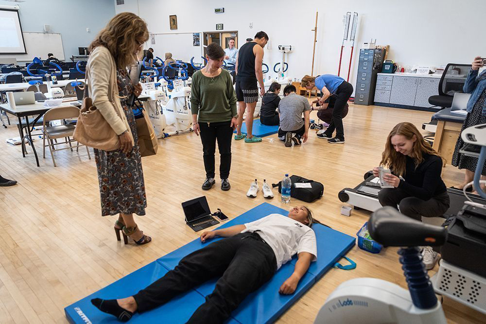 The president watching a student lay on a yoga matt at the college of health and human sciences tour.